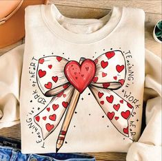 a t - shirt with hearts and pencils on it sitting next to some jeans