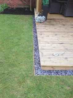 a wooden deck in the middle of a yard with grass and gravel on the ground