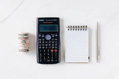 a calculator, notepad and pen on a white table with a notebook