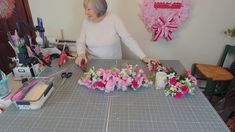 an older woman is cutting flowers on a table with scissors and other crafting supplies