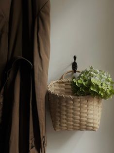 a wicker basket hanging on the wall next to a coat rack with flowers in it