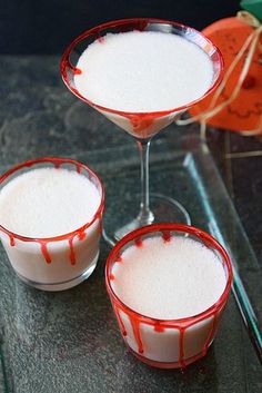 three glasses filled with white liquid sitting on top of a glass table next to an orange pumpkin