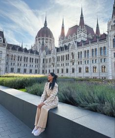 a woman sitting on a ledge in front of a large building with towers and spires