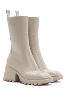 The rubber Betty rain boot reveals a sleek, strong upper recalling classic leather boots and incorporating the Maison's signature contours. The voluntarily oversized back loop shows the Chloé logo, while an internal zipper closure ensures a fitted, feminine silhouette. Short and flat, the square toe shape lends a strong, assertive attitude. The comfortable heel elevates the silhouette, while the bold lugged sole gives an edgy attitude to this rain boot. Chloe Rain Boots, Chloe Betty Boots, Pvc Boots, Chloe Logo, Chloe Clothing, Beige Boots, Boots Beige, Wellington Boots, Comfortable Heels