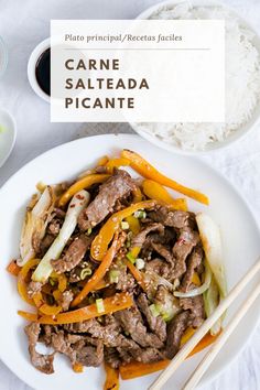 a white plate topped with meat and veggies next to chopsticks on top of rice