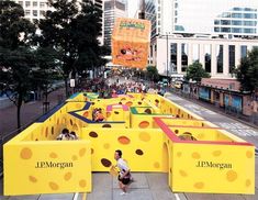 people are walking on the sidewalk in front of large yellow blocks that look like cheese