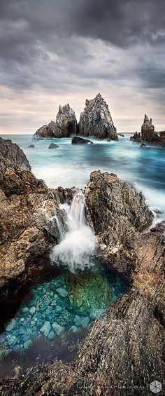 an ocean scene with rocks and water in the foreground, under a cloudy sky