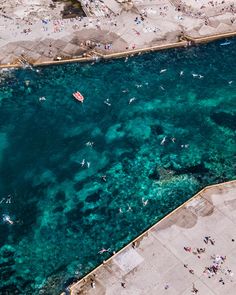 an aerial view of people swimming in the blue water near a beach with several small boats