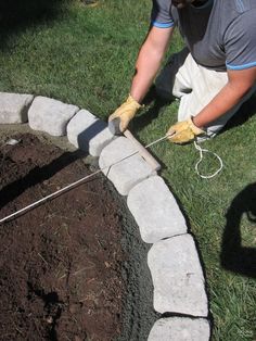 a man is working on some kind of stone wall in the grass with his hands