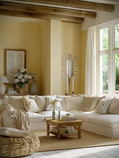 a living room filled with lots of white furniture and large windows covered in sunlight shining through the curtains