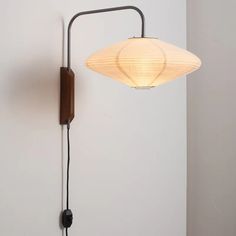 a wall lamp with a white shade on it and a black cord hanging from the side