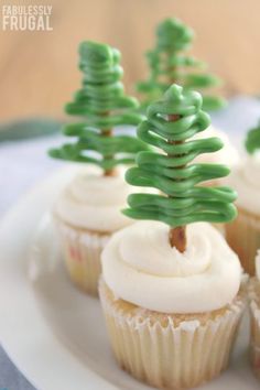 cupcakes decorated with green icing and trees on top are sitting on a white plate