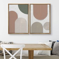 two paintings hang on the wall above a wooden table in a living room with white chairs