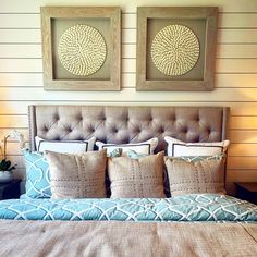 a bed with two framed pictures above it and pillows on the headboard, in front of a wooden paneled wall