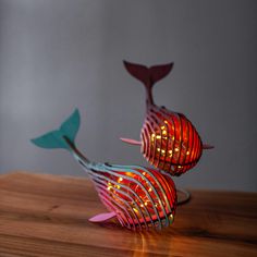 two colorful metal fish sculptures sitting on top of a wooden table next to each other