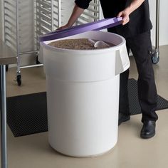 a man standing next to a large white trash can filled with sand and plastic spoons