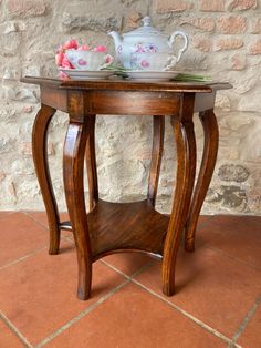 a wooden table with a tea pot on top and flowers in the vase next to it