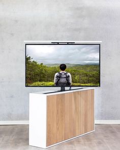 a man sitting on top of a wooden cabinet in front of a flat screen tv