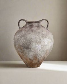 an old gray vase sitting on top of a white table next to a light colored wall