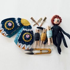 an assortment of crafting supplies including scissors, yarn and doll's clothes on a white surface