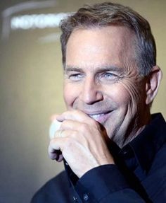 a close up of a person wearing a black shirt and smiling at the camera with his hand on his chin