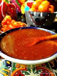 a bowl filled with red sauce sitting on top of a table next to oranges