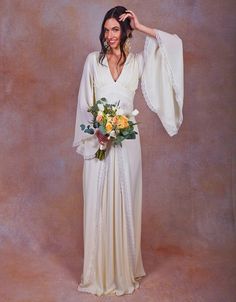 a woman in a white dress holding a bouquet and wearing a shawl over her shoulder