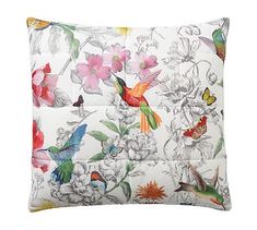 a white pillow with colorful birds and flowers on the front, along with two different colored hummingbirds