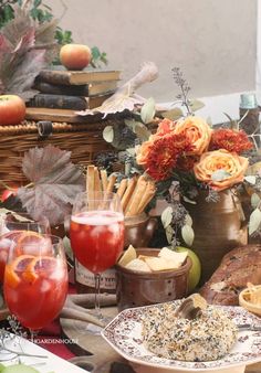 an assortment of food and drinks on a table in front of books, flowers, fruit, and other items