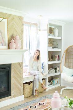 a woman sitting on a bench in front of a fire place and bookshelf