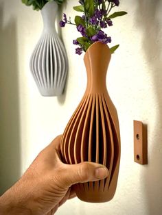 a hand holding a vase with flowers in it next to a wall mounted light switch