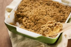 a wooden spoon is in a green casserole dish with crumbs on it