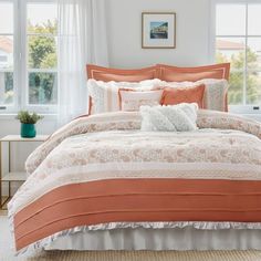 an orange and white comforter set in a bedroom next to two windows with curtains