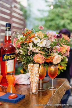 a table topped with two vases filled with flowers next to bottles of alcohol and glasses