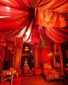 a bed room with lots of red and gold draping on the ceiling,