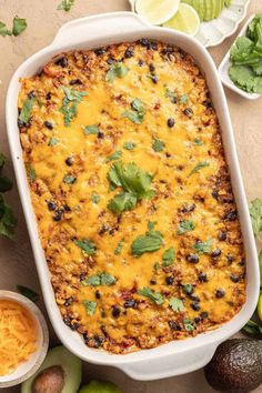 an enchilada casserole in a white dish surrounded by avocados and limes