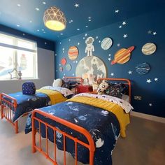 two beds in a room with blue walls and outer planets painted on the wall behind them