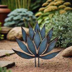 a metal plant sitting on top of a dirt ground next to some rocks and plants