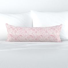 a white bed topped with pillows and a pink pillow on top of it's headboard