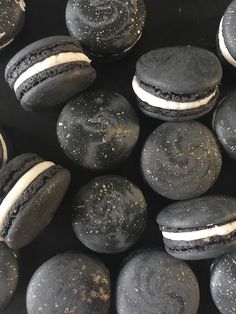 black macaroons with white frosting and sprinkles are shown here