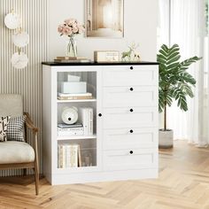 a white cabinet with drawers in a living room next to a chair and potted plant