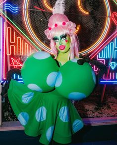 a woman dressed in green and white polka dot dress standing next to a neon sign