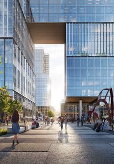 people are walking through an open area in front of tall buildings with glass windows on each side