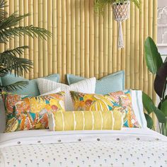 a bed with colorful pillows and blankets in front of a bamboo headboard that has plants hanging on it