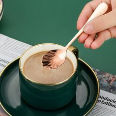 a person holding a spoon over a cup of coffee on top of a green saucer