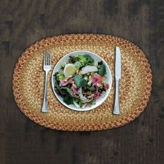 a white plate topped with salad on top of a wooden table next to a fork and knife