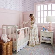 a woman standing next to a baby crib in a pink room with blue and white wallpaper