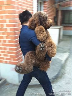 a man carrying a large teddy bear on his back in front of a brick building