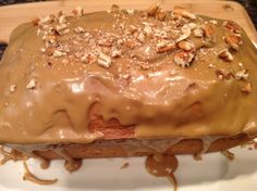 a cake covered in frosting and nuts on top of a white plate with a wooden cutting board