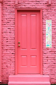 a bright pink door and bench in front of a brick wall with a sign on it